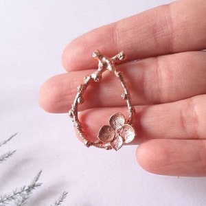 Pu&ograve; includere: Un ciondolo in oro rosa con un delicato design floreale. Il ciondolo ha la forma di un ramo con un piccolo fiore al centro.