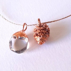 Puede incluir: Un collar delicado con dos colgantes: un cristal de cuarzo transparente y una piña de pino de color cobre.