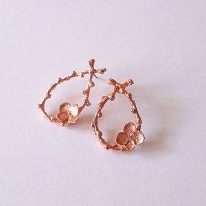 Pu&ograve; includere: Un paio di orecchini in rame con un delicato design floreale. Gli orecchini hanno la forma di un cerchio con un piccolo fiore al centro.