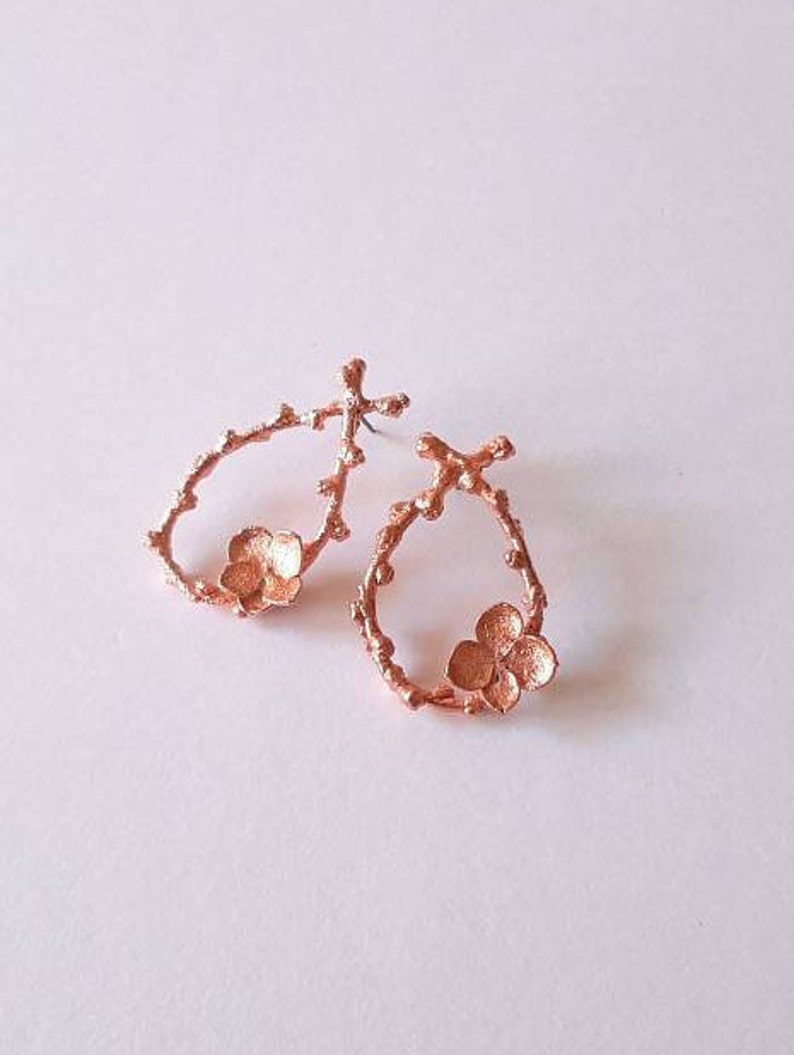 Pu&ograve; includere: Un paio di orecchini in rame con un delicato design floreale. Gli orecchini hanno la forma di un cerchio con un piccolo fiore al centro.