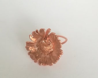 Op de afbeelding: Een koperen ring met een bloemmotief. De bloem is gedetailleerd en heeft een textuur.