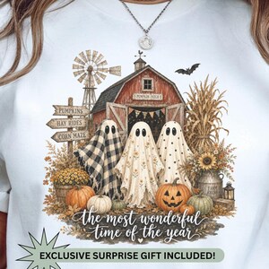 May include: A white t-shirt featuring a graphic of three ghosts in front of a red barn, a windmill, and pumpkins. The text reads "the most wonderful time of the year" and "EXCLUSIVE SURPRISE GIFT INCLUDED!" with signs for "PUMPKINS," "HAY RIDES," and "CORN MAZE."