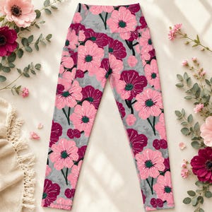 Può includere: Leggings a vita alta con motivo floreale. I leggings presentano uno sfondo grigio con fiori rosa e bordeaux. I fiori hanno centri verdi. I leggings hanno una tasca laterale.