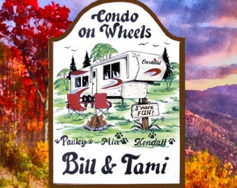 May include: A hand-painted wooden sign with a cartoon illustration of a camper, a campfire, and two chairs. The sign reads "Condo on Wheels" and "Bill & Tami". The camper has the word "Cardinal" on the side. There are three paw prints with the names "Paisley", "Mia", and "Kendall" below the camper.