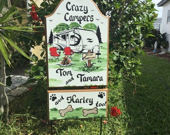 May include: A two-part wooden sign with the words "Crazy Campers" and a drawing of a camper, campfire, and two red chairs. The sign also includes the names "Tom and Tamara" and "Harley too!"