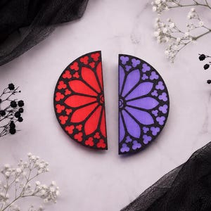 Könnte beinhalten: Zwei halbkreisförmige Dekorationsobjekte mit schwarzem Rahmen und gotischem Rosenfenstermuster. Ein Teil hat eine leuchtend rote, durchscheinende Einlage, während das andere eine violette Einlage aufweist, was einen Buntglaseffekt erzeugt.