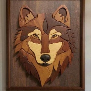 Pode incluir: Arte de parede em madeira com o rosto de um lobo, feito de vários tons de madeira. A obra de arte apresenta um mosaico detalhado de peças castanhas claras e escuras, com um nariz preto e olhos de cor clara. A peça é emoldurada em uma borda castanha escura.