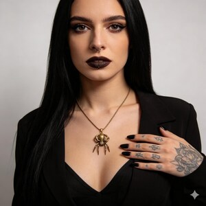 May include: A gold-colored spider pendant necklace. The spider has detailed legs and a round body. The necklace is worn on a black blazer. The background is a plain white.
