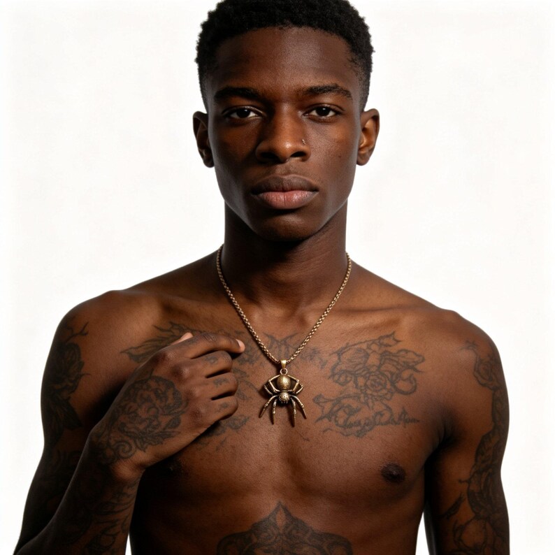 May include: A gold-colored spider pendant necklace. The pendant is a detailed depiction of a spider. The necklace is worn by a person with tattoos on their chest and arms. The background is plain white.