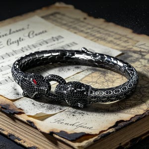 May include: A silver bracelet with a panther head design. The panther heads are encrusted with black stones and have red eyes. The bracelet has a hexagonal pattern and is resting on a vintage sheet of music.