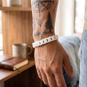 May include: A white chain link bracelet featuring thick, interlocking matte links that wrap around the wrist. The bracelet has a uniform, smooth finish and a substantial, bold design that sits securely on the arm.