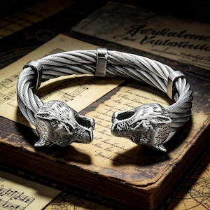 May include: A silver bracelet with a woven cable design. The ends of the bracelet are sculpted as wolf heads. The bracelet is presented on an antique book with aged paper and musical notation.