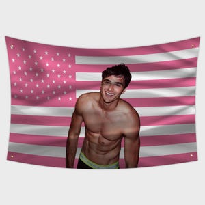 May include: A pink American flag tapestry with white stars and stripes. A smiling person is in front of the flag, wearing black underwear with a yellow waistband.