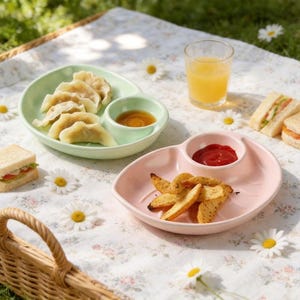 Puede incluir: Una escena de picnic con dos platos divididos: uno verde con empanadillas y salsa, y otro rosa con patatas fritas y ketchup. Un vaso de zumo de naranja y sándwiches también están presentes sobre una manta floral.