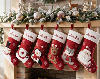 May include: Six red Christmas stockings with white cuffs, each embroidered with the name Aurelia. The stockings feature appliqued characters including a snowman, polar bear, penguin, reindeer, fox, and Santa Claus, all accented with white snowflakes.
