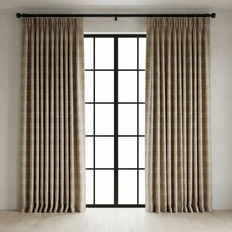 May include: Two beige plaid curtains hang on a black rod above a black-framed window. The curtains are pleated and have a subtle grid pattern. The window is divided into multiple panes, and the floor is light-colored wood.
