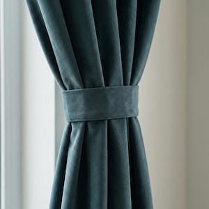 May include: Teal velvet curtains with a matching tieback. The curtains are draped and gathered, showcasing the soft texture and rich color. The tieback is a simple band that holds the curtains in place, creating a classic and elegant look for any room.