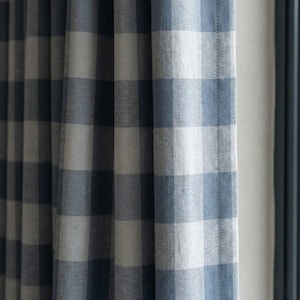Può includere: Primo piano di una tenda a quadri blu e bianchi. Il tessuto ha un aspetto strutturato, con i quadri in diverse tonalità di blu e bianco. La tenda è appesa, con morbide pieghe.