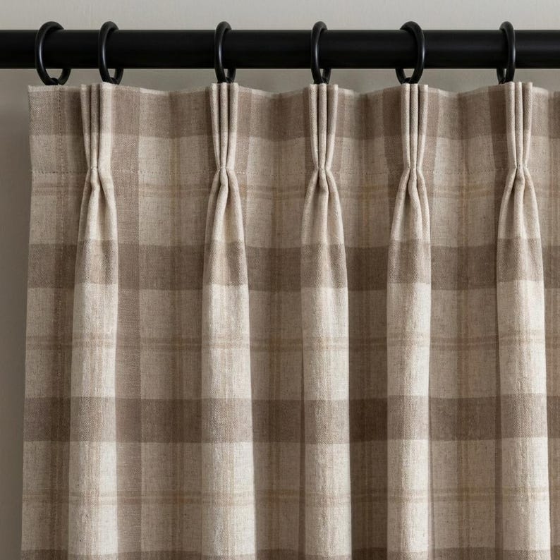 May include: Beige and brown plaid curtain panels hanging from a black metal rod with black rings. The curtains are pleated and have a textured appearance. The plaid pattern is a classic design, suitable for various interior styles.
