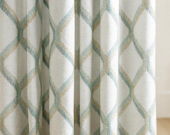 May include: White curtain with a repeating diamond pattern. The pattern is made up of interwoven lines in shades of blue and tan. The curtain is made of a textured fabric.