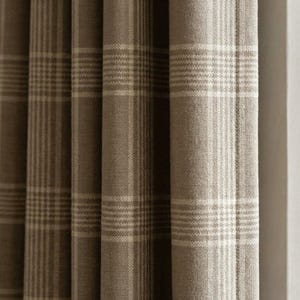 May include: Close-up of a set of brown and beige plaid curtains. The fabric has a textured appearance with vertical folds. The plaid pattern consists of alternating stripes of brown and beige, creating a classic and neutral design for home decor.