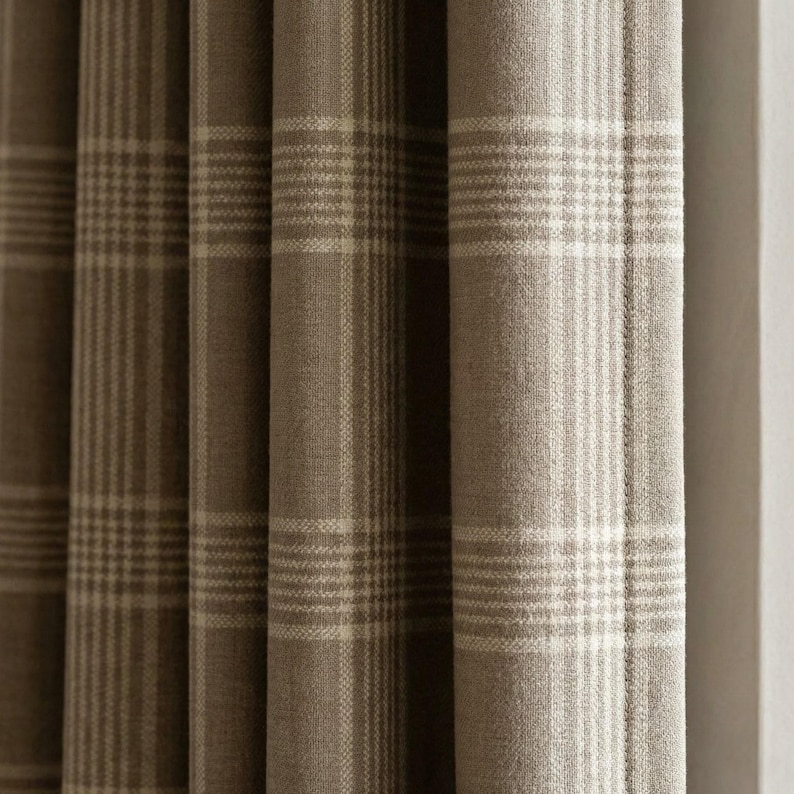 May include: Close-up of a set of brown and beige plaid curtains. The fabric has a textured appearance with vertical folds. The plaid pattern consists of alternating stripes of brown and beige, creating a classic and neutral design for home decor.