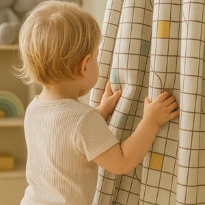 Könnte beinhalten: Ein junges Kind mit blondem Haar, das ein geripptes Kurzarm-Shirt trägt, betrachtet einen beigen Vorhang. Der Vorhang hat ein Gittermuster mit braunen, gelben und blaugrünen Quadraten. Das Kind hält den Vorhang mit beiden Händen.