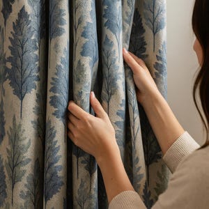 Könnte beinhalten: Vorhangstoff mit einem sich wiederholenden Baumblattmuster in Blau- und Grautönen. Der Stoff hat einen neutralen Hintergrund, wobei das Blattmuster für visuelles Interesse sorgt. Der Vorhang wird gehalten, um die Textur und den Fall des Stoffes zu zeigen.