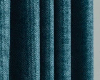 May include: Close-up of teal fabric curtains with a textured weave. Vertical folds create shadows, highlighting the woven pattern. The curtains are a solid colour, suitable for home decor.