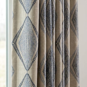 Peut inclure: Un panneau de rideau beige orné d'un motif répétitif en losange brodé avec du fil bleu foncé. La broderie se compose de boucles complexes et interconnectées qui remplissent les formes en losange, créant un aspect texturé sur le tissu.