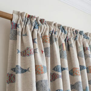 May include: Beige linen curtains with a repeating pattern of colorful fish in blue, orange, and red. The curtains are gathered at the top and hang in soft folds. The fish design adds a nautical theme to the room.