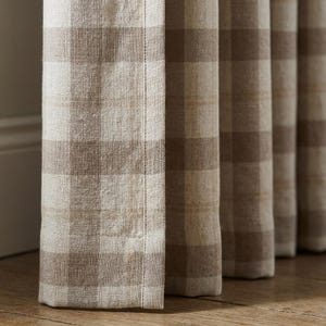 May include: Close-up of beige and brown checkered curtains. The fabric has a textured appearance, with visible threads and a subtle sheen. The curtains are hanging vertically, with a visible seam down the side.