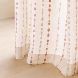 May include: Off-white linen curtain featuring vertical rows of peach and sage green embroidered dots. The curtain has a neutral colour palette and a simple, elegant design. The bottom edge has a matching border.