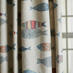 May include: Beige fabric curtain with a repeating pattern of stylized fish in shades of blue, red, and orange. The fish designs vary in pattern and size, creating a whimsical, nautical theme. The curtain is made of a textured fabric.