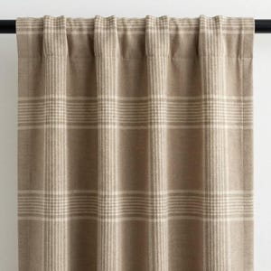 May include: Tan and cream plaid curtain panel. The curtain features a classic plaid pattern with horizontal and vertical lines. The fabric is a neutral color, suitable for various interior design styles. The curtain is hanging from a black rod.