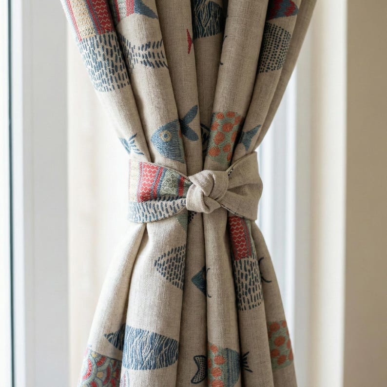 May include: Beige linen curtains with a repeating pattern of stylized fish in blue, red, and orange. The curtains are tied back with a matching fabric tie, creating a decorative knot. The curtains are hanging in front of a window.