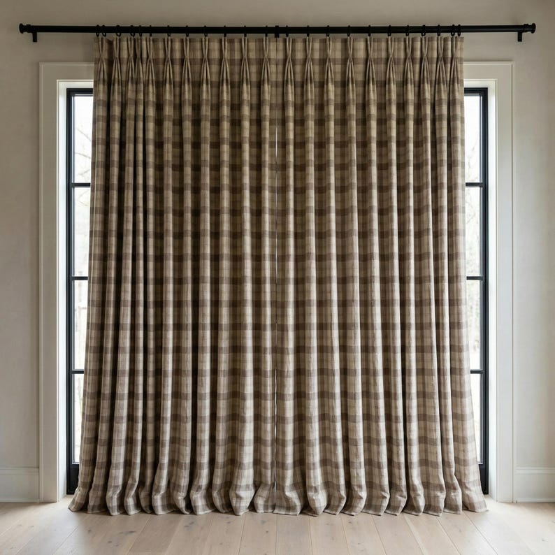 May include: Full-length, pleated window curtains in a neutral plaid pattern. The curtains are primarily beige and brown, with a subtle grid design. They hang from a black rod above a window with a black frame. The curtains are floor-length and create a soft, textured look.