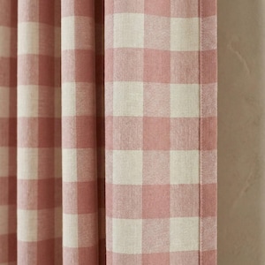 May include: Close-up of a pink and white checkered curtain panel. The fabric has a woven texture, with the pink squares slightly darker than the white squares. The curtain is hanging, with vertical folds visible.