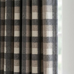May include: A curtain panel featuring a large-scale buffalo check pattern in shades of charcoal grey, light grey, and beige. The fabric has a visible woven texture with vertical pleats that create deep folds, hanging straight down.