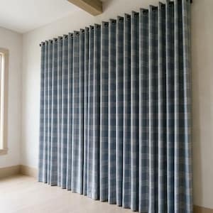 May include: Blue and white plaid curtains hanging from a rod with black grommets. The curtains are floor-length and cover a large portion of a white wall. The room has light-colored wood flooring and a window.