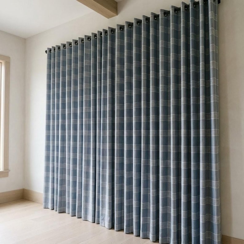 May include: Blue and white plaid curtains hanging from a rod with black grommets. The curtains are floor-length and cover a large portion of a white wall. The room has light-colored wood flooring and a window.