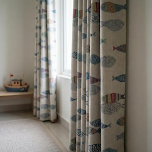 May include: Beige linen curtains with a repeating pattern of colorful fish in blue, red, and green. The curtains are hanging in front of a window, with a small wooden boat visible in the background. The curtains add a nautical theme to the room.