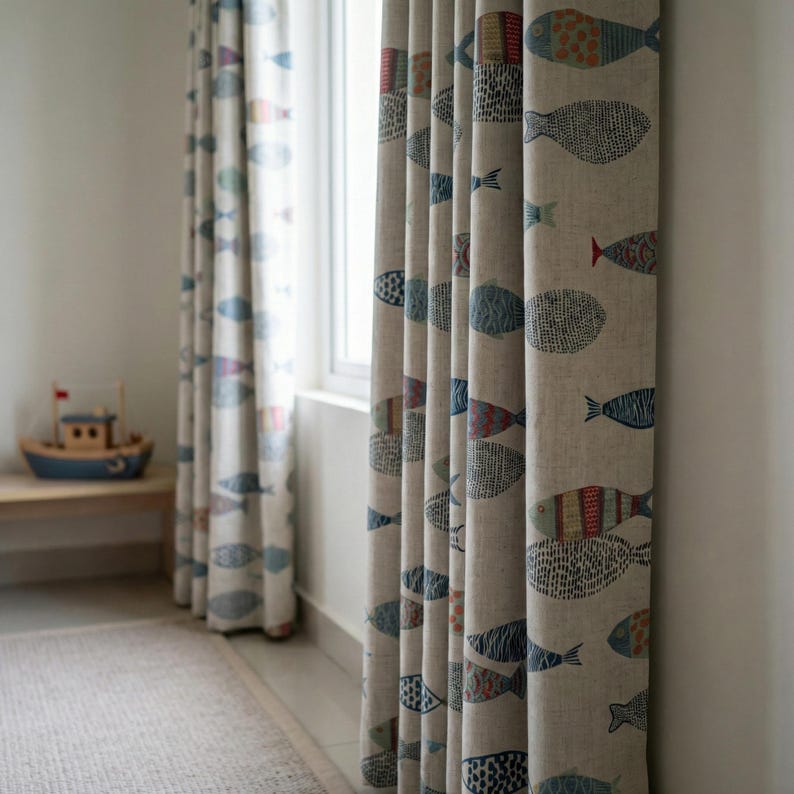 May include: Beige linen curtains with a repeating pattern of colorful fish in blue, red, and green. The curtains are hanging in front of a window, with a small wooden boat visible in the background. The curtains add a nautical theme to the room.