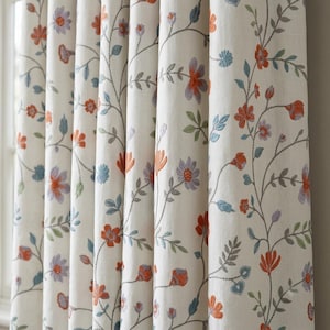 May include: An off-white curtain panel featuring a repeating embroidered pattern of climbing vines with small leaves and flowers in shades of orange, light blue, and lavender. The fabric has a visible weave texture and hangs in vertical folds.
