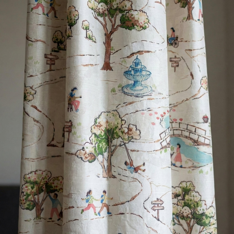 May include: Cream-colored fabric curtain with a whimsical park scene print. The design features winding paths, trees, a fountain, and figures engaged in various activities. The color palette includes shades of green, brown, blue, and pink.
