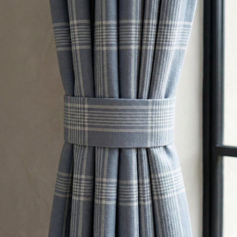 May include: Blue plaid curtains with a matching fabric tie-back. The curtains are a light blue color with a white plaid pattern. The tie-back is a solid light blue color with a white plaid pattern.
