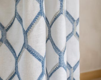 Könnte beinhalten: Weiße Stoffvorhänge mit einem geometrischen Rautenmuster in Blau und Grau. Die Vorhänge bestehen aus einem strukturierten Material und hängen in weichen Falten, wodurch ein dekoratives Element für ein Fenster entsteht.