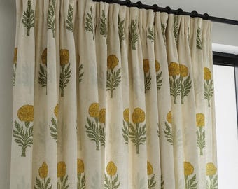 Könnte beinhalten: Cremefarbene Blumenvorhänge mit einem sich wiederholenden Muster aus gelben Blumen und grünen Blättern. Die Vorhänge hängen an einer schwarzen Stange und sind in weichen Falten drapiert, was einen strukturierten Look erzeugt.