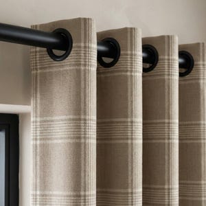 May include: Close-up of beige plaid curtains with black grommets and a black curtain rod. The curtains have a neutral color palette with a grid pattern. The window treatment is a home decor item.