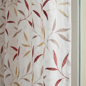 Puede incluir: Panel de cortina blanco con diseño de hojas bordadas. Las hojas son en tonos rojos, dorados y marrones. La cortina tiene costuras verticales y está colgada frente a una ventana.